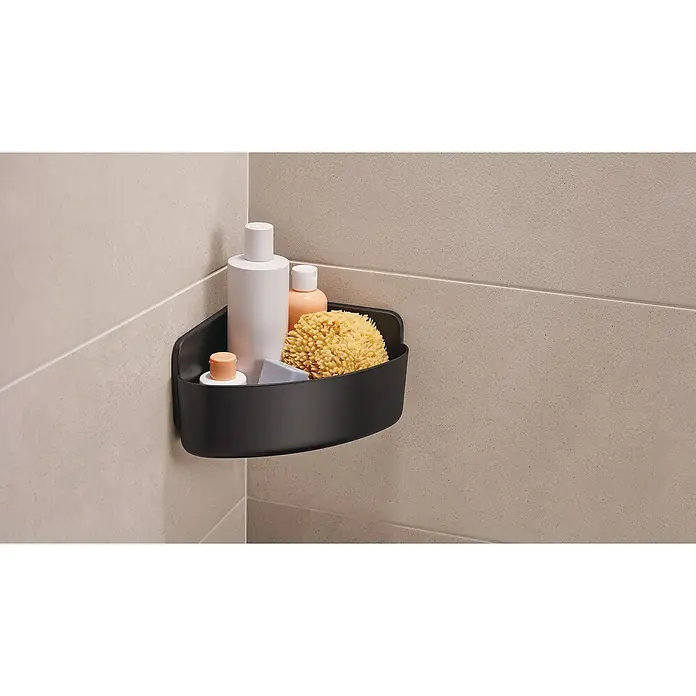 Tesa Cesta de baño angular Lavaa M - 20 x 20 x 12 cm, Plástico, Negro - Un estante de esquina negro con varios productos de baño en una pared de azulejos, que ofrece una solución de almacenamiento práctica.