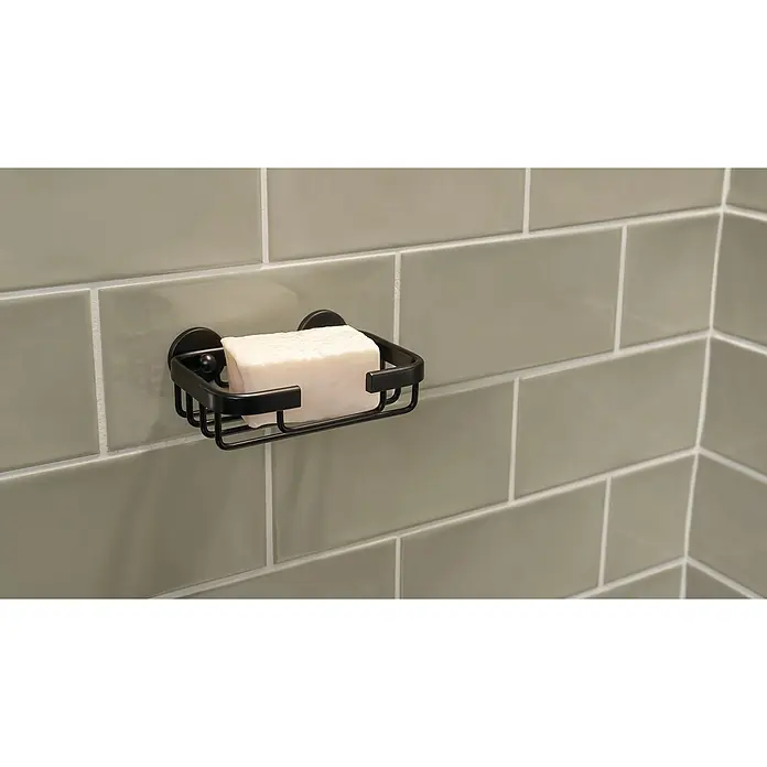 Tesa Aluxx Jabonera Aluxx - 9,5 x 13,5 x 4,7 cm, Aluminio, Cromo - Una pastilla de jabón rectangular se encuentra en una jabonera de alambre negro adherida a una pared de azulejos grises.