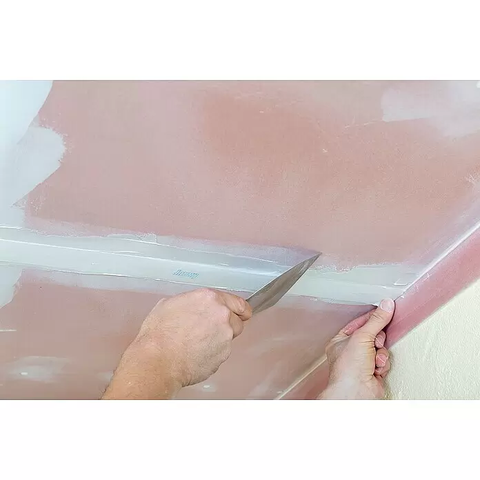Knauf Fugenspachtel Leicht - 10 kg - Eine Person trägt weiße Spachtelmasse und Fugenband auf rosa Trockenbau-Deckenfugen mit einem Spachtel auf.