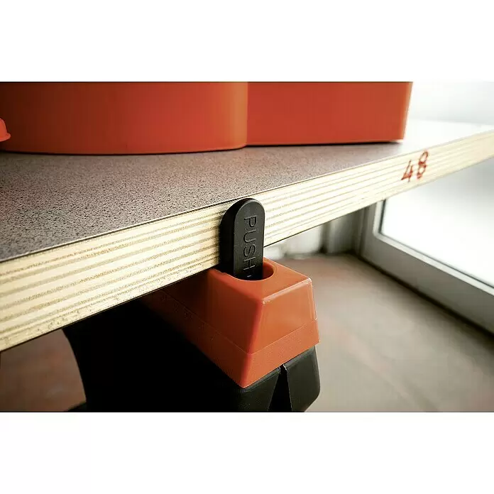 Lockweiler Unterstellbock SH 020 - Belastbarkeit: 200 kg, 2 Stk. - Orange-schwarze Klemme sichert ein Holzregal mit grauer Oberfläche, mit schwarzem 'PUSH'-Hebel.