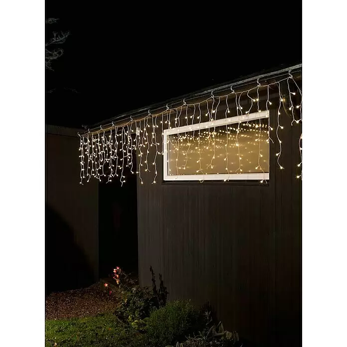Konstsmide LED-Lichtervorhang Eisregen - Außen, 15,07 m, Warmweiß, 200 Stk., Netzbetrieben - Warmweiße Eiszapfen-Lichterkette an dunkler Dachrinne, die Fenster und Garten bei Nacht beleuchtet.