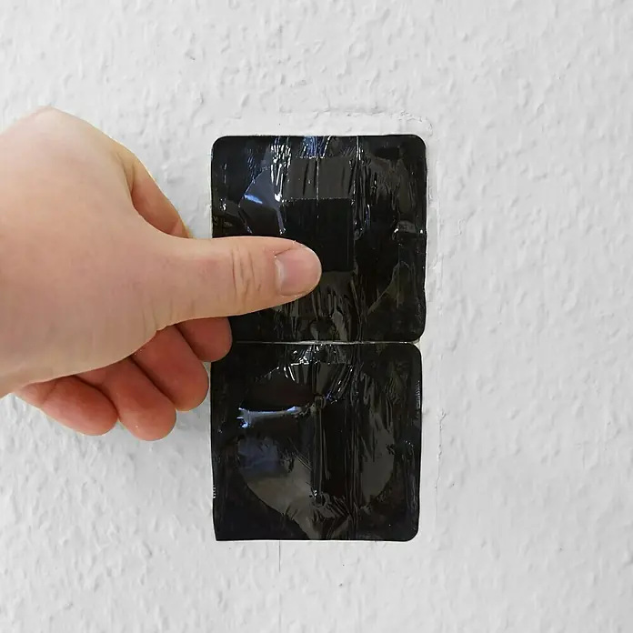 Mako Abdeckband - 70 x 70 mm - Nahaufnahme eines Mannes, der einen schwarzen, rechteckigen, abdeckenden Aufkleber von einer weißen Wand entfernt.