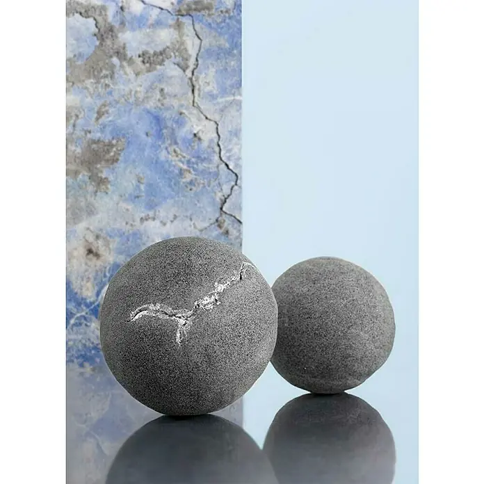 Glorex Hobby Time Modelliermasse Betonplast - Betongrau, 500 g - Zwei graue Kugeln, eine mit einem silbernen Riss, auf einer reflektierenden Oberfläche vor einem blauen Hintergrund.