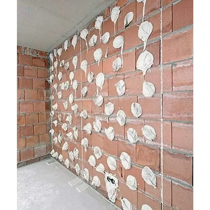Knauf Ansetzgips Perlfix - 25 kg, Geeignet für: Gipsplatten - Nahaufnahme einer Ziegelwand mit Gipsflecken, die die Vorbereitung für die Verkleidung zur Wärmeisolierung zeigt. Perfekt für Bau- und Renovierungsprojekte.