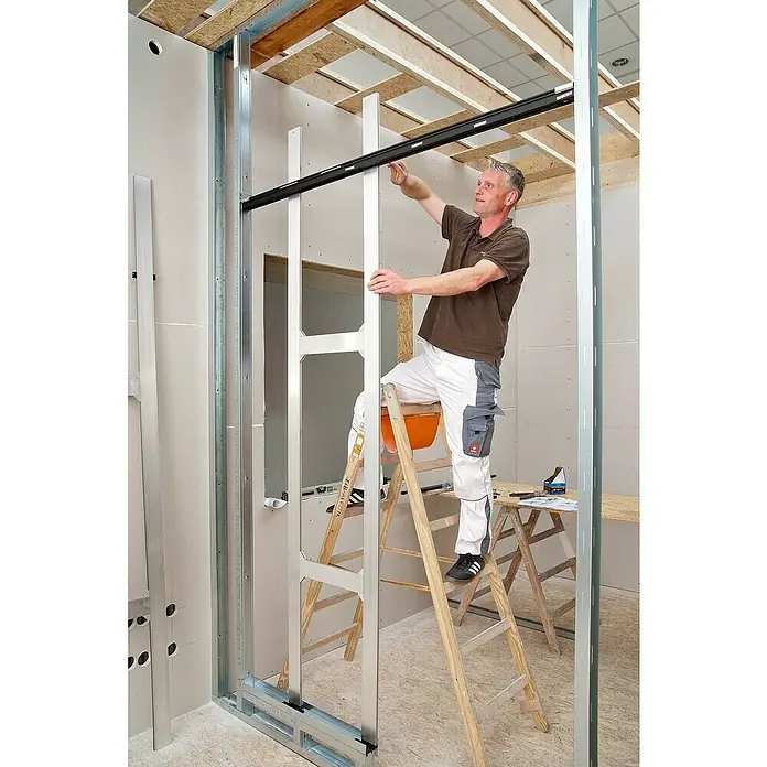 Knauf Klemmbacken Pocket Kit - Belastbarkeit pro Tür: 120 kg, Passend für: Glastürblätter mit Glasdicken 8/10/12 mm VSG/ESG - Ein Handwerker montiert ein Trockenbausystem mit Metallrahmen und Gipskartonplatten. Der Fokus liegt auf dem innovativen Wandaufbau.