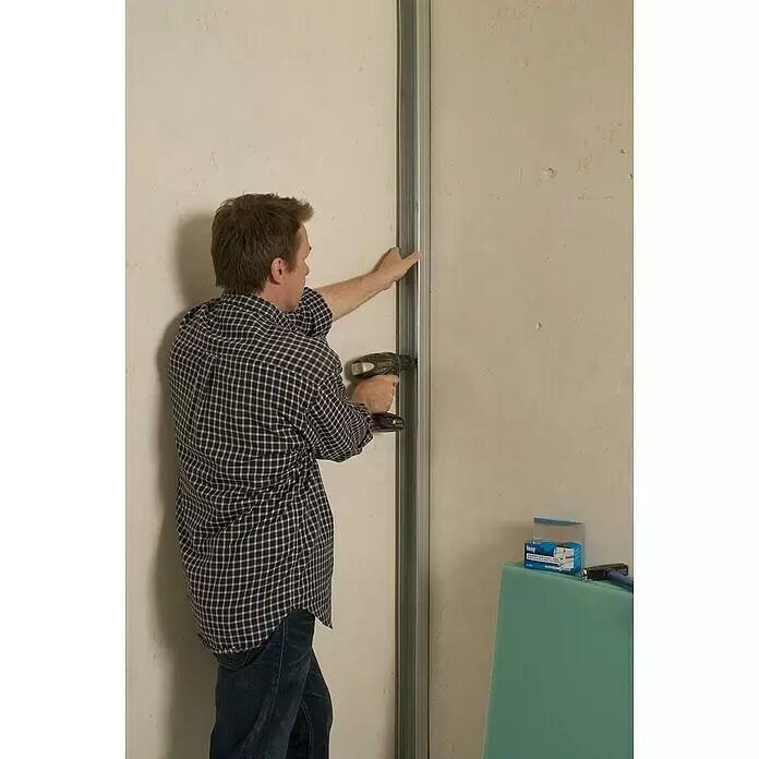 Knauf Schnellbauschraube TN 35 - Durchmesser: 3,9 mm, Länge: 35 mm, 250 Stk. - Mann montiert mit einem Akkuschrauber ein Metallprofil an einer Wand. Grüne Gipskartonplatten und Baumaterialien liegen rechts.