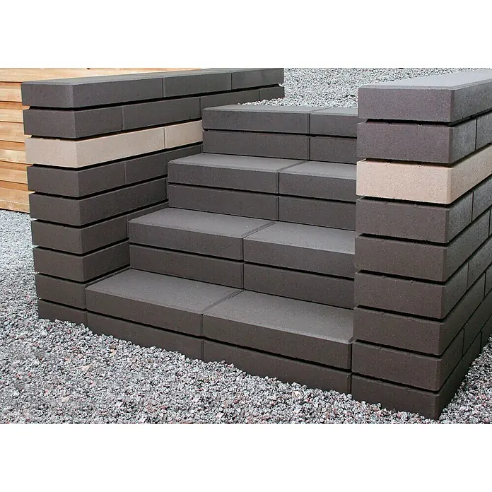 Christoph Mauerstein C-Line - Grau, 50 x 25 x 10 cm, Beton - Eine Treppe aus dunklen Pflastersteinen mit hellen Akzenten, umgeben von Kies, vor einem unscharfen Holzhintergrund.