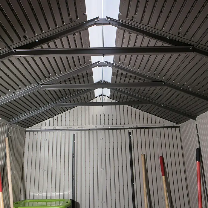 Gerätehaus Phoenix - Außenbreite inkl. Dachüberstand: 206 cm, Außentiefe inkl. Dachüberstand: 280 cm, Kunststoff, Lichtgrau/Anthrazit - Innenansicht eines Gartenhauses mit Oberlichtern und Werkzeugen, die an der Wand lehnen. Das Design sorgt für viel Tageslicht.