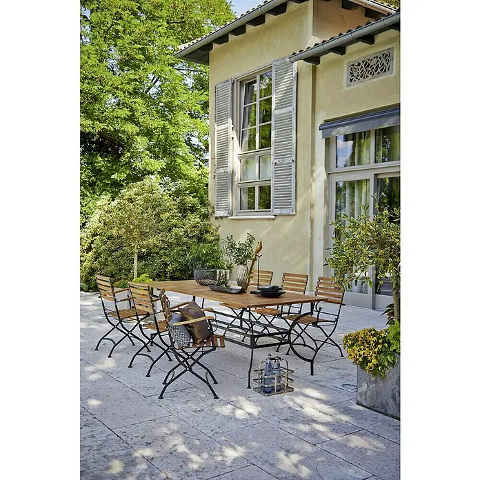 Sunfun Moni Gartentisch - L x B x H: 220 x 100 x 77 cm - Ein einladender Außenbereich mit einem eleganten Esstischset aus Holz und Metall, umgeben von üppigem Grün.
