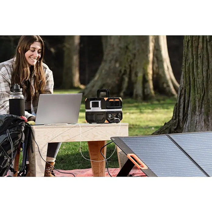 Technaxx Powerstation TX-201 - 315 Wh, Schwarz - Frau arbeitet im Freien mit einem Laptop, der an eine tragbare Powerstation und ein Solarpanel angeschlossen ist.