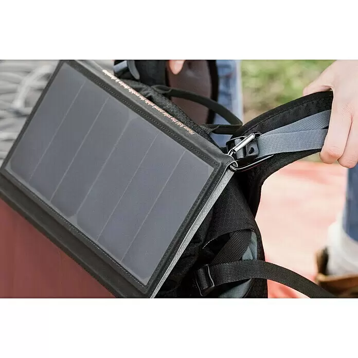 Yard Force Solar-Powerbank LX PB21 - 48,1 Wh, 65 x 28,5 x 1,5 cm - Tragbares graues Solarpanel mit Karabiner an einem schwarzen Rucksack befestigt, von einer Hand gehalten, bereit zum mobilen Laden im Freien.
