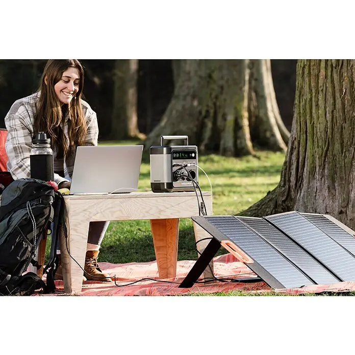 Yard Force Powerstation LX PS600 - 518 Wh, Nennleistung: 600 W, Max. Leistung: 1.200 W - Frau arbeitet im Freien mit einer Blackforce Powerstation und Solarpanel, die ihren Laptop mit Strom versorgt.