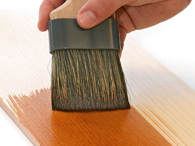 Hand streicht Holz mit Lasur
