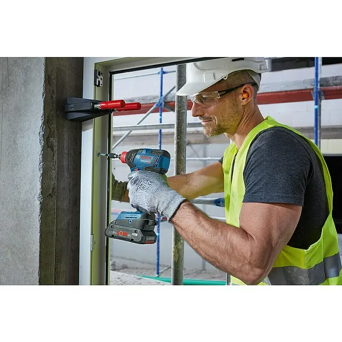 Bosch Professional Set de taladros GDX18V-200+GSB18V-55 - 18 V, 2 baterías, 4 Ah, 5 pzs. - Primer plano de un obrero de la construcción que utiliza un atornillador de impacto inalámbrico Bosch para fijar tornillos en un marco de ventana.