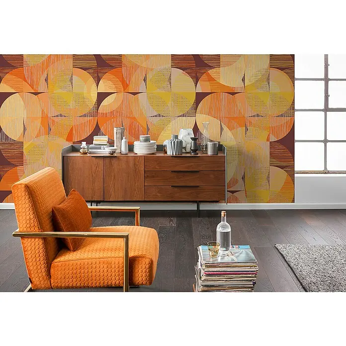 Komar Infinity 2 Fototapete Seventies Swing - B x H: 300 x 250 cm, Vlies - Wohnzimmer mit orangefarbenem Sessel und Holzkommode vor einer Wand mit geometrischem Muster, das ein modernes und warmes Ambiente schafft.