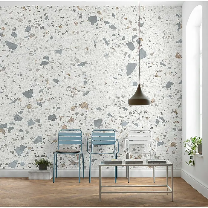 Komar Infinity 2 Fototapete Terrific Terrazzo - B x H: 400 x 250 cm, Vlies - Die Aufnahme zeigt drei Stühle und einen Couchtisch vor einer Terrazzo-Wand, beleuchtet von einer Hängelampe. Die Szene ist hell und einladend.