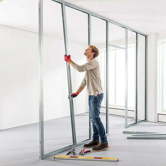 Probau CW-Standprofil - 3.500 x 100 x 50 mm - Ein Mann montiert eine Metallständerwand. Das Produkt ist ein Metallrahmen für den Innenausbau mit Werkzeug im Raum.