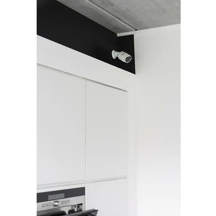 Chacon Cámara de vigilancia falsa exterior - Blanco - Una cámara de seguridad blanca está montada en un techo negro sobre armarios de cocina blancos con un diseño elegante.