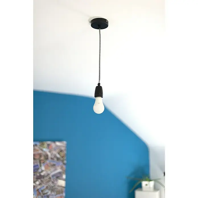 Chacon Casquillo cerámico - Cerámica, Negro, 1 ud. - Primer plano de una bombilla colgando del techo con cable textil, ideal para diseño minimalista e iluminación ambiental.