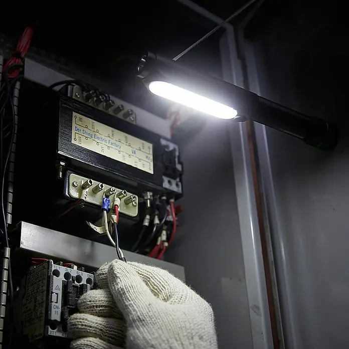 GP Taschenlampe C34 - 85 lm - 550 lm, IPX4 - Eine Arbeitsleuchte beleuchtet eine Schalttafel, während eine Hand mit einem Handschuh an den Drähten arbeitet.