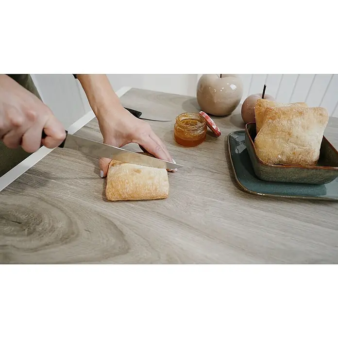 Mesa de jardín Mistral - L x An x Al: 192 x 102 x 74 cm, Aluminio/Cerámica, Antracita - Una persona corta pan con un cuchillo sobre una mesa de madera al lado de mermelada, platos y decoraciones de frutas.