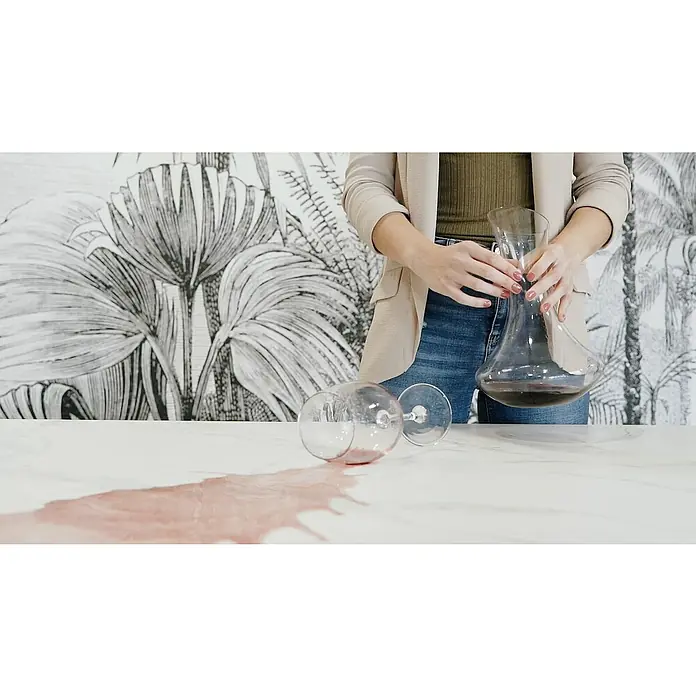 Mesa de jardín Mistral - L x An x Al: 192 x 102 x 74 cm, Aluminio/Cerámica, Antracita - Una copa de vino volcada derrama vino tinto sobre una mesa, mientras una persona sostiene un decantador de vino cerca.