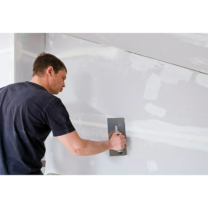 Knauf Feinspachtel Uniflott Finish - 4 kg, Gebrauchsfertig - Ein Mann glättet eine Wand mit einem Spachtel, um eine glatte Oberfläche für die Endbearbeitung zu schaffen. Der Spachtel ist das Hauptwerkzeug.