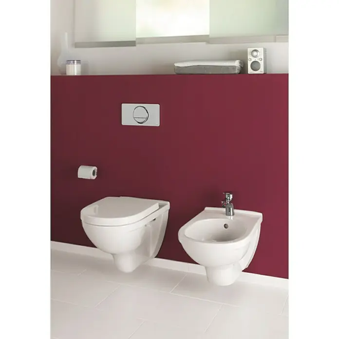 Villeroy & Boch O.novo Wand-WC-Set - Spülrandlos, Mit schmutzabweisender Glasur, Spülform: Tief, WC Abgang: Waagerecht, Weiß - Moderne Toilette und Bidet an einer weinroten Wand. Die weißen Sanitärkeramiken stehen auf hellen Fliesen und wirken sehr elegant.