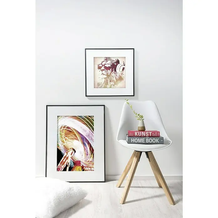 Nielsen Alurahmen C2 - 60 x 80 cm, Schwarz - Ein modernes Interieur mit zwei gerahmten Kunstwerken und einem stilvollen weißen Stuhl mit Holzbeinen, dekoriert mit Büchern und einer kleinen Vase.