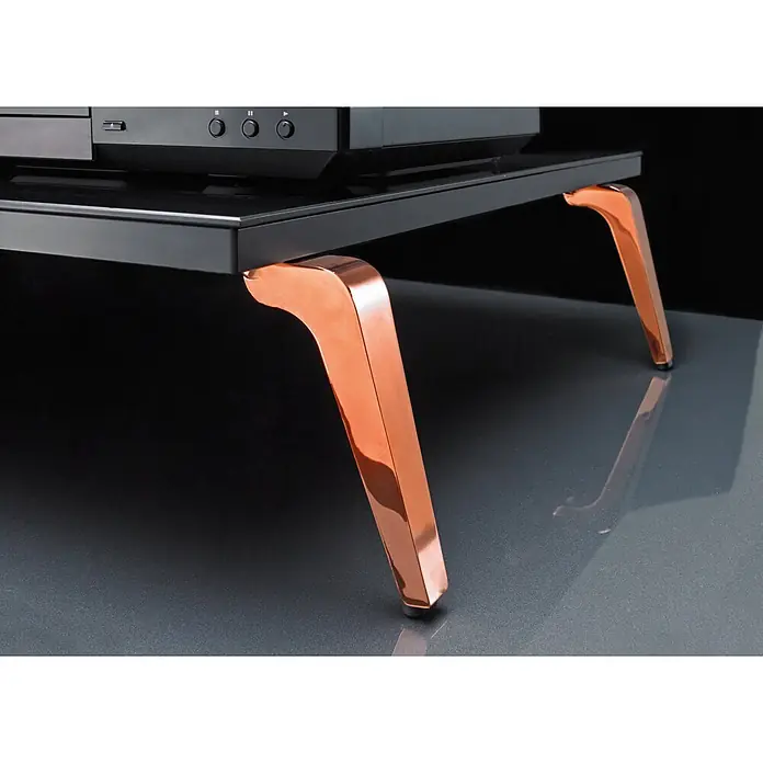 Hettich Möbelfuß Lanoia - L x B x H: 7 x 7,7 x 17 cm, Traglast: 50 kg, Stahl, Kupfer - Nahaufnahme eines schwarzen Medienregals mit glänzenden Kupferbeinen. Das Regal steht auf einer reflektierenden Oberfläche vor einem dunklen Hintergrund.