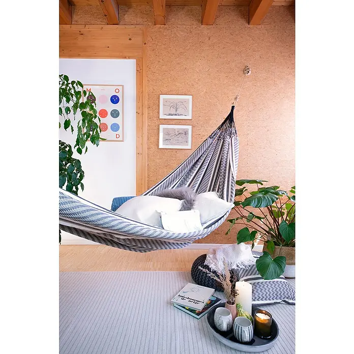 La Siesta Doppelhängematte Flora - L x B: 350 x 160 cm, Zebra, Ausführungseigenschaft: Double - Das Bild zeigt eine stilvolle Hängematte mit Kissen in einem gemütlichen Raum, dekoriert mit Pflanzen und einer Leseecke, die zum Entspannen einlädt.