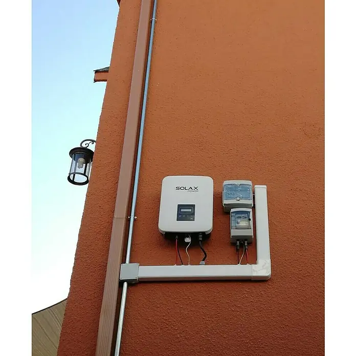 Inversor X1 Boost - 5 kW, L x An x Al: 14,3 x 43 x 34,15 cm - Un inversor Solax Power y las cajas eléctricas asociadas están montados en una pared con una lámpara exterior.