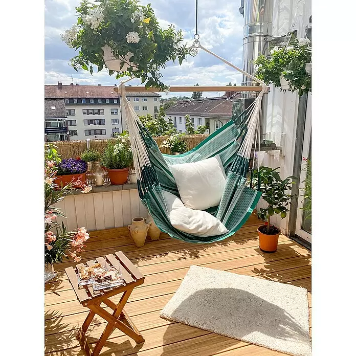La Siesta Hängesessel Habana Comfort - L x B x H: 180 x 115 x 160 cm, Agave - Grün-weiß gestreifter Hängesessel mit weißen Kissen, an einer Holzstange auf einem hellen Balkon mit Pflanzen und Holzfußboden, lädt zur Entspannung ein.