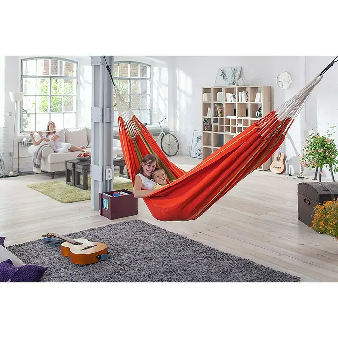 La Siesta Doppelhängematte Flora - L x B: 400 x 180 cm, Chili, Ausführungseigenschaft: Kingsize - Kinder entspannen in einer farbenfrohen Hängematte, die im hellen Wohnzimmer zwischen zwei Säulen aufgehängt ist. Gemütliche Atmosphäre mit Gitarre und Teppich.