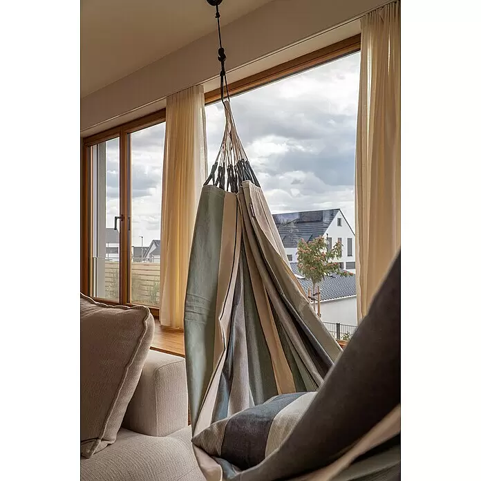 La Siesta Hängematte Modesta - L x B: 350 x 160 cm, Olive, Double - Gestreifter Hängesessel in Grün-, Beige- und dunklen Tönen, hängt drinnen neben einem Fenster und Sofa.