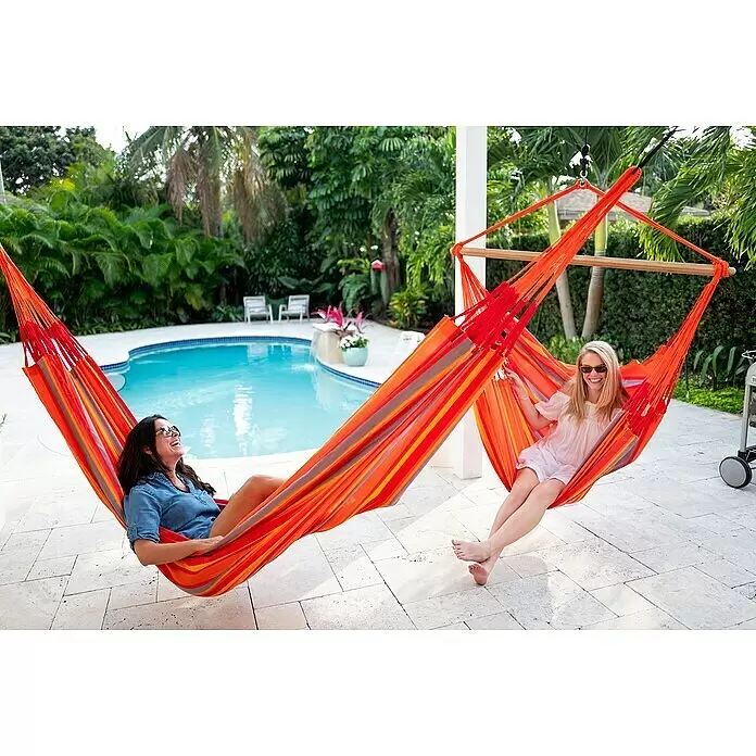 La Siesta Hängesessel Domingo Kingsize - Toucan - Zwei gestreifte Hängematten in Rot, Orange, Gelb, Grau, mit Frauen, die am Pool entspannen.