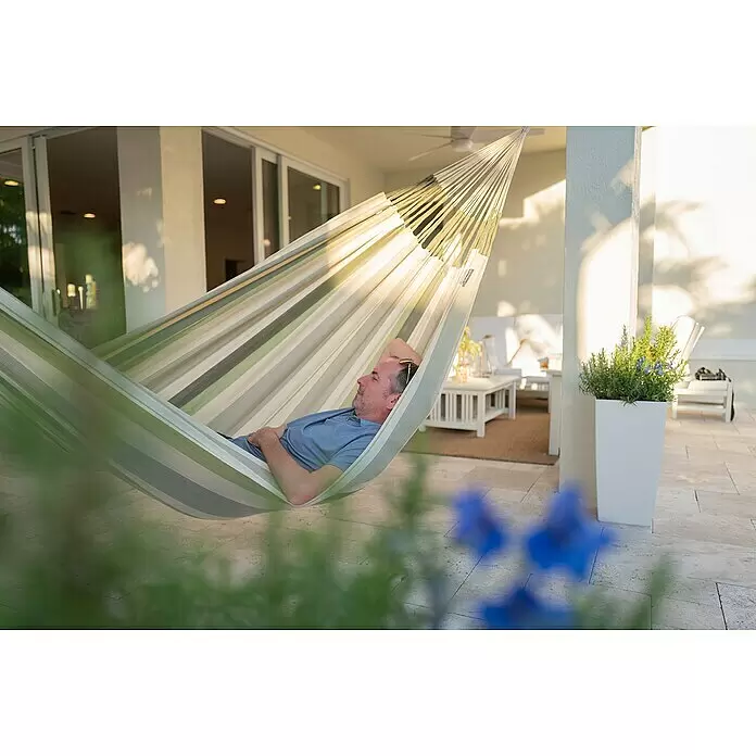 La Siesta Hängematte Brisa Kingsize - L x B: 400 x 180 cm, Cedar - Mann entspannt sich in einer gestreiften Stoffhängematte auf einer Terrasse.