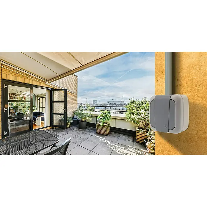 Siemens Delta IP54 Feuchtraum-Steckdose SIE028660 - 1-fach, IP54, Grau - Außenaufnahme einer grau-weißen Außensteckdose, die an einer senffarbenen Wand auf einer Terrasse montiert ist.