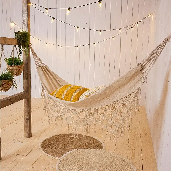 Hamaca individual Bali - L x An: 290 x 100 cm, Arena - Hamaca acogedora con borlas, cojines amarillos y alfombras de yute bajo luces, creando un ambiente relajante.
