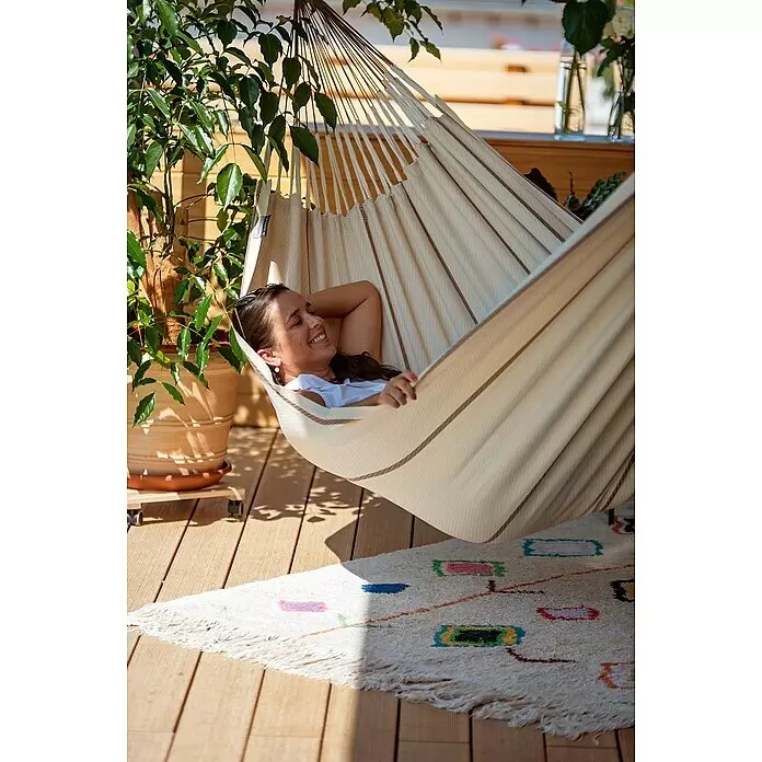 La Siesta Hängematte Modesta - L x B: 350 x 160 cm, Nougat, Double - Eine Frau entspannt in einer hellen Stoffhängematte mit braunen Streifen auf einer sonnigen Terrasse.