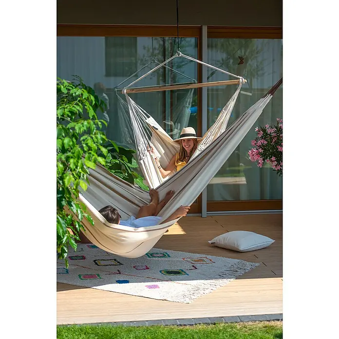 La Siesta Hängematte Modesta - L x B: 350 x 160 cm, Nougat, Double - Eine Frau mit Hut und ein Kind entspannen in einer Doppelhängematte auf einer Terrasse. Die Hängematte hängt von einer Holzkonstruktion.