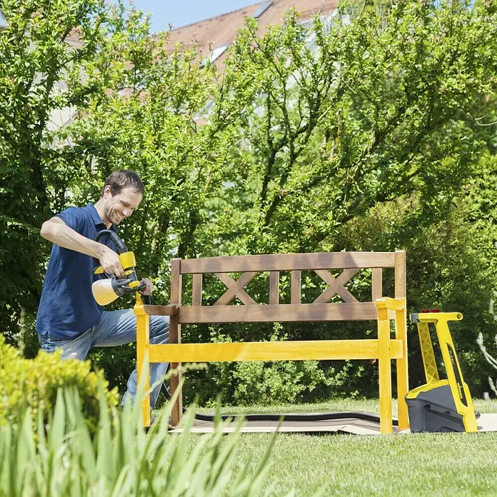 Wagner Farbsprühsystem W 950 Flexio - 630 W, Förderleistung: 0,525 l/min - Mann lackiert eine Holzbank mit dem Farbsprühsystem WAGNER, das neben der Bank auf einer Pappe steht.