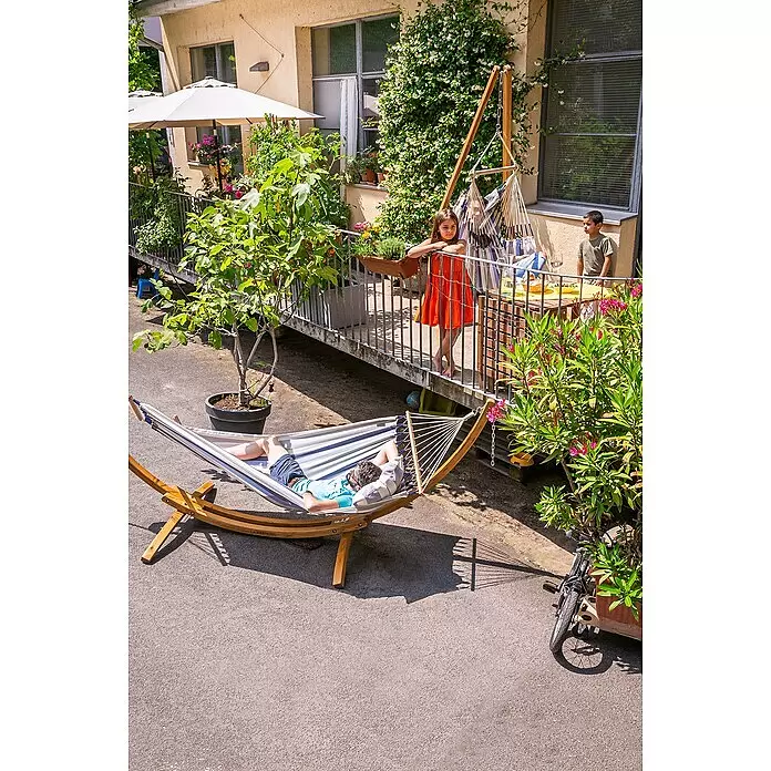 La Siesta Stabhängematte Alisio - L x B: 300 x 140 cm, Sea Salt, Single - Ein Mann entspannt in einer gestreiften Hängematte mit stabilem Holzgestell, draußen auf einer Terrasse.