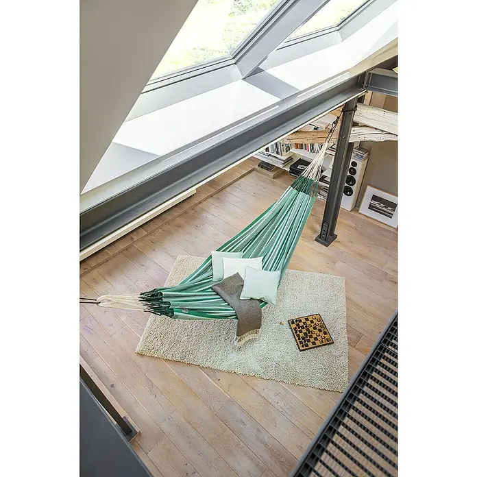 La Siesta Hängematte Modesta - L x B: 400 x 180 cm, Agave, Kingsize - Grün-weiß gestreifte Hängematte mit Kissen auf einem Teppich in einem hellen Raum mit Dachfenstern.