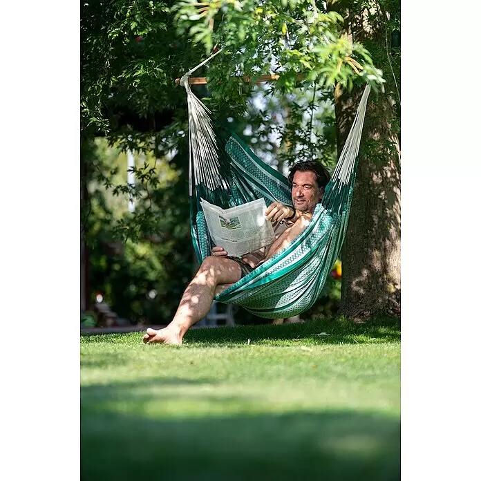 La Siesta Hängesessel Habana Kingsize - L x B x H: 210 x 130 x 170 cm, Agave - Ein Mann entspannt in einer grün-weiß gestreiften Hängematte und liest Zeitung im Garten.