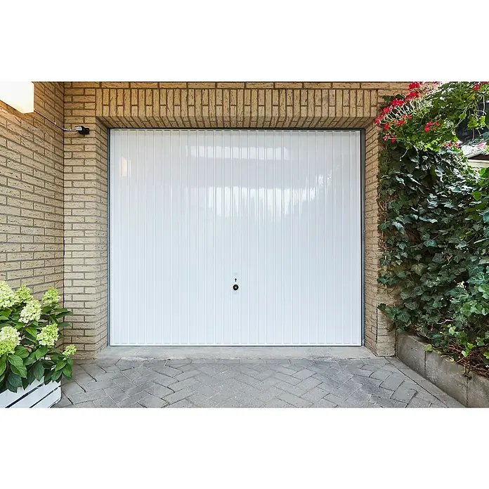 swingcolor Weißlack Kunstharz - Weiß, Hochglänzend, 750 ml, Lösemittelbasiert - Ein weißes Garagentor aus Metall mit vertikalen Rillen, eingebettet in eine Backsteinfassade, umrahmt von Pflanzen.