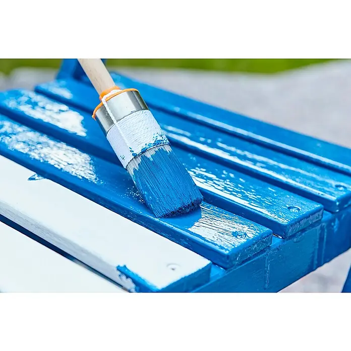swingcolor Buntlack Kunstharz für Außen - Enzianblau, Seidenmatt, 2,5 l, Lösemittelbasiert - Ein Pinsel trägt blaue Farbe auf eine Holzbank auf. Der Pinsel ist mit blauer Farbe bedeckt und die Bank ist teilweise blau gestrichen.