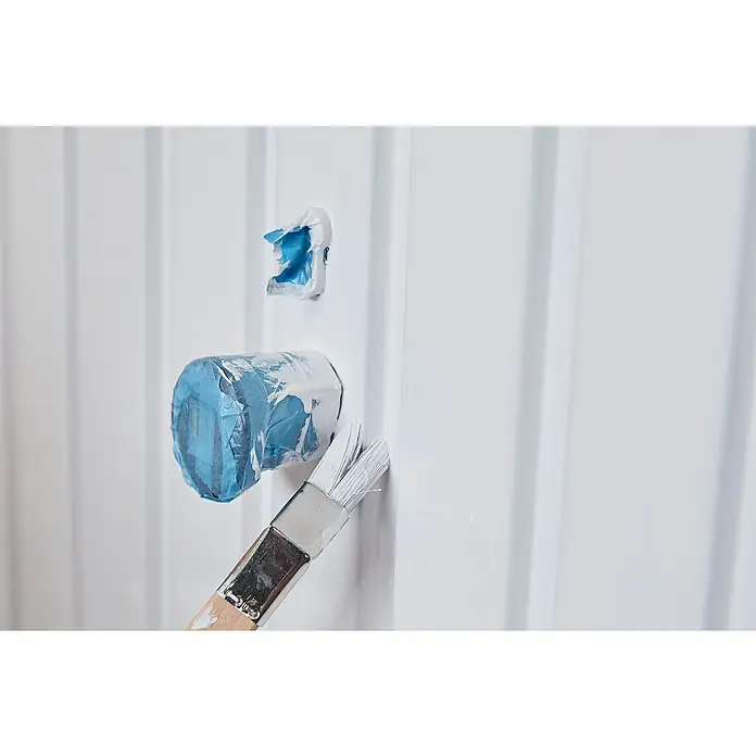 swingcolor Weißlack Kunstharz - Weiß, Hochglänzend, 750 ml, Lösemittelbasiert - Nahaufnahme einer weißen Wand, die mit weißer Farbe und einem Pinsel gestrichen wird, wobei ein Steckdose mit blauem Klebeband abgedeckt ist.