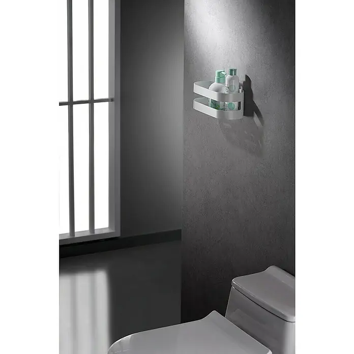 Imex Cesta de baño Nirmala - 10,4 x 25 x 9 cm, Acero inoxidable, Blanco - Una moderna estantería esquinera blanca de dos niveles sostiene botellas en una pared gris en un baño de diseño minimalista.
