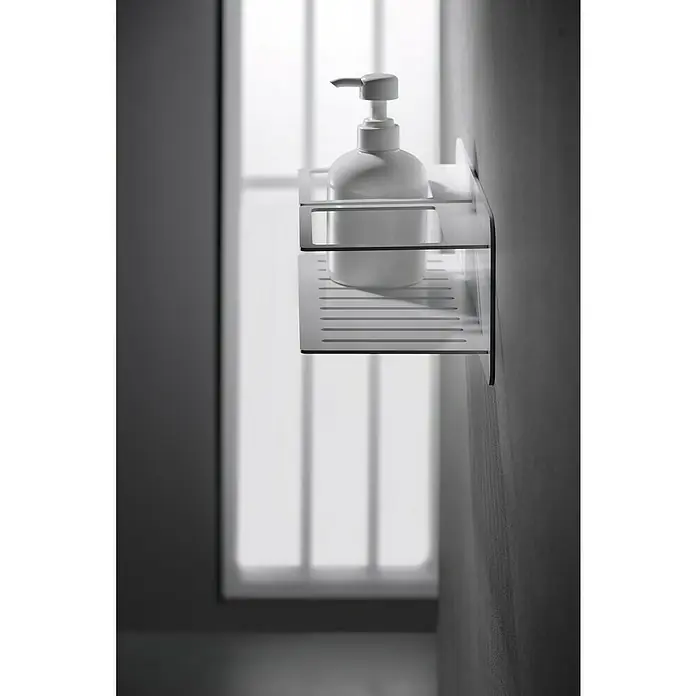 Imex Cesta de baño Iman - 12,7 x 36 x 13,5 cm, Acero inoxidable, Blanco - Primer plano de una botella de jabón blanca en una estantería con diseño de láminas fijada a una pared cerca de una ventana.
